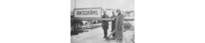 Svartvitt foto. Tre män som står bredvid varandra nära en skylt med text: Riksgräns.